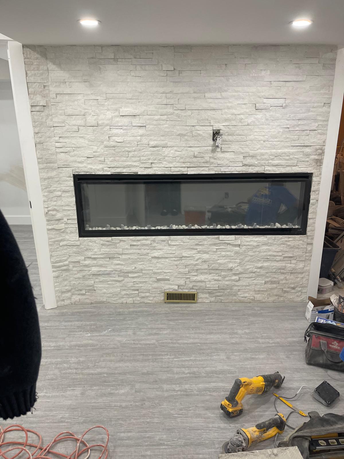 Finished stacked white stone feature wall with a linear electric fireplace and grey plank flooring