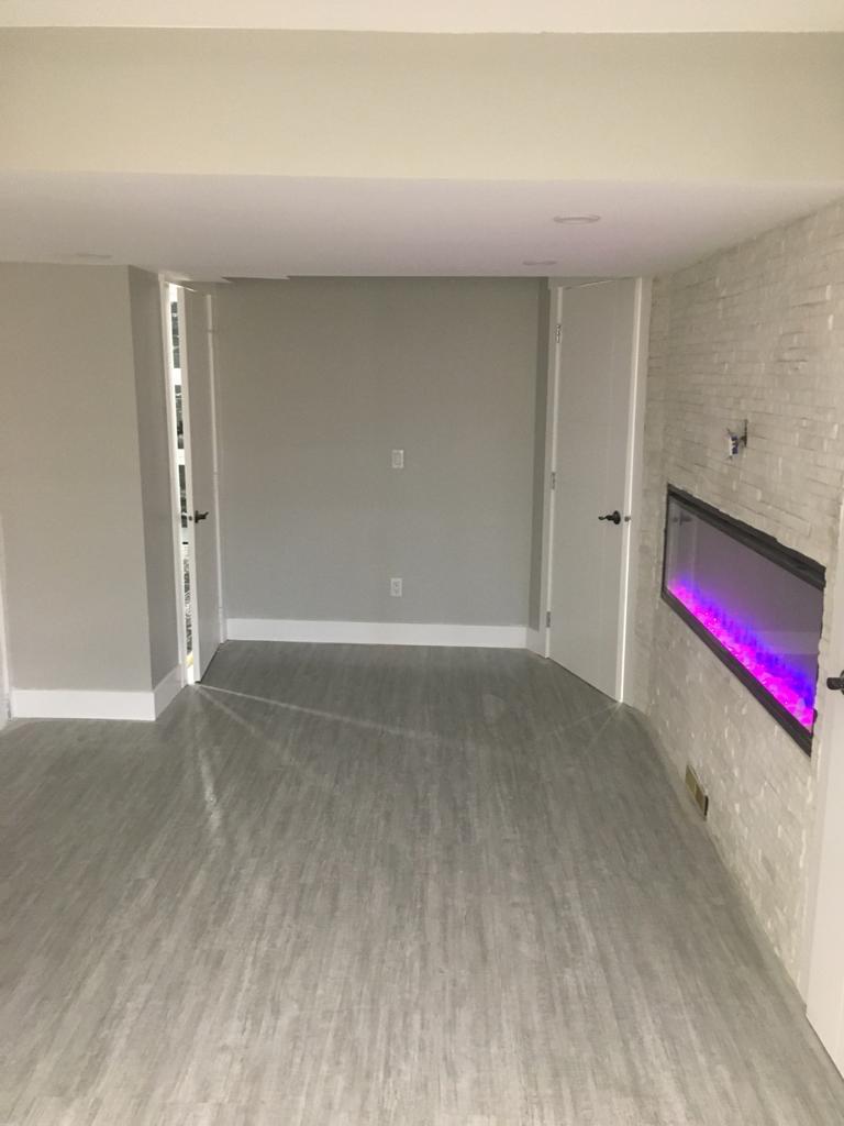 Completed basement living area with painted walls, white doors, plank flooring and a wall fireplace