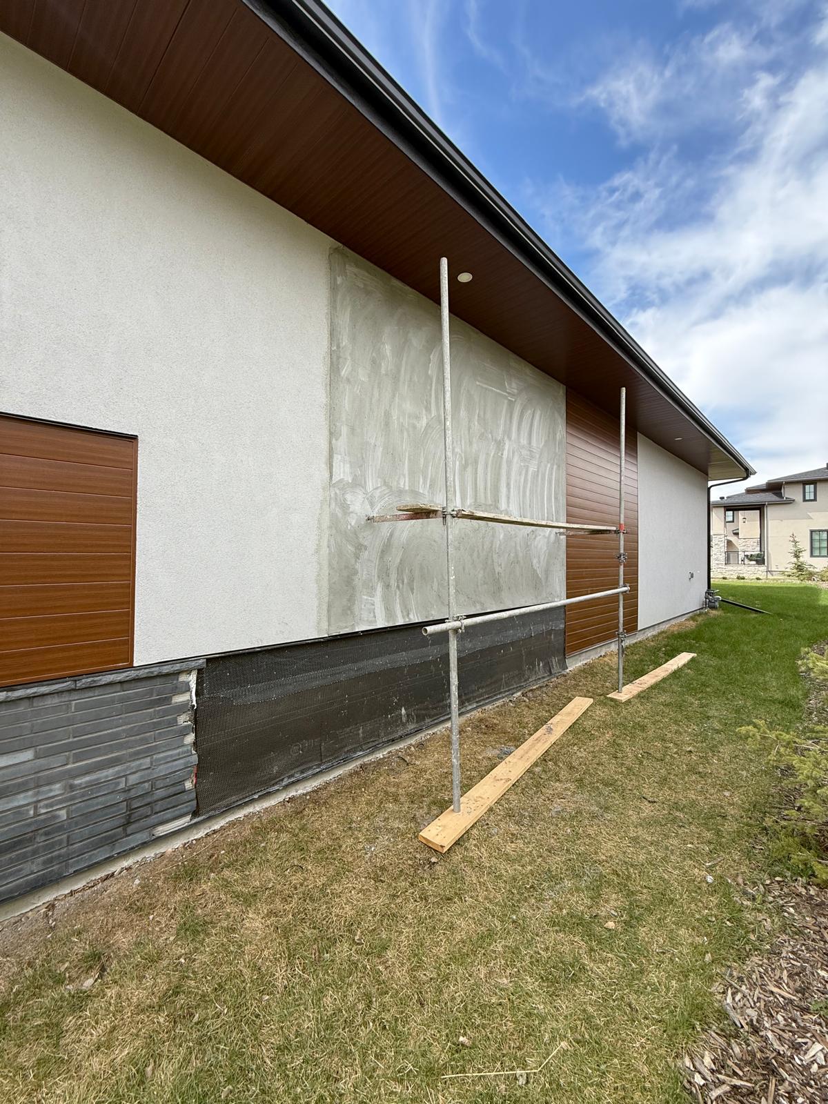 Exterior stucco repair in progress with scaffolding beside cedar-tone siding