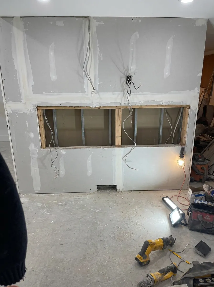 Unfinished basement wall with bare drywall, a framed fireplace opening and exposed wiring